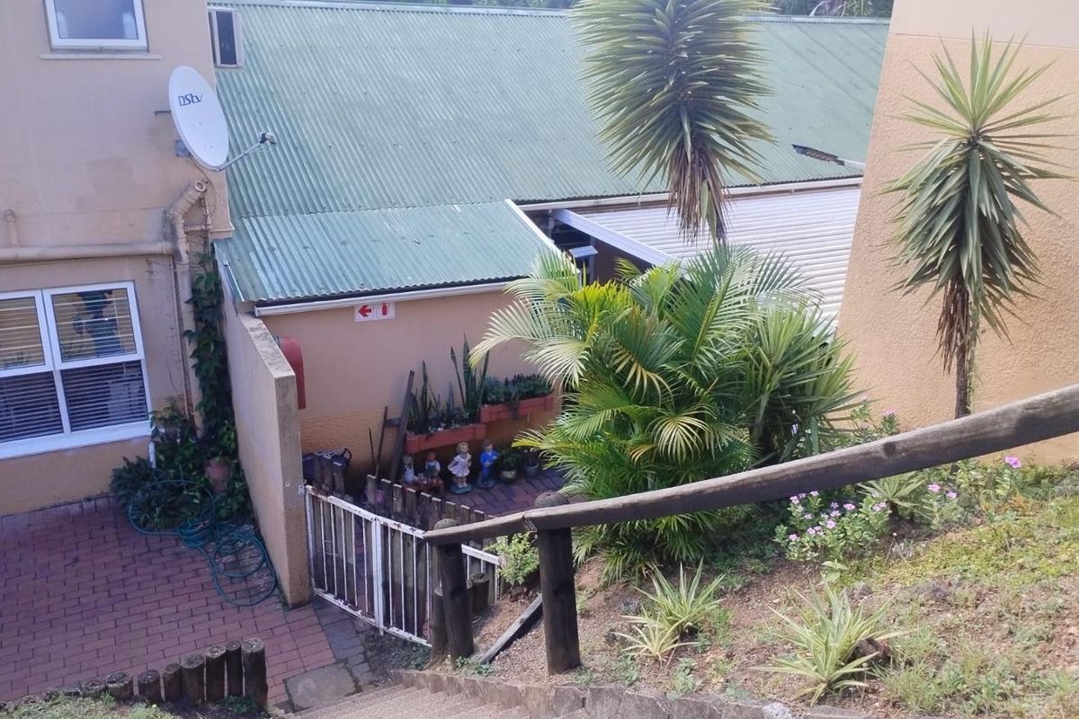Rear view of the townhouse showing a paved courtyard area, corrugated metal roofing, and concrete stairs with a timber handrail leading down to the garden.