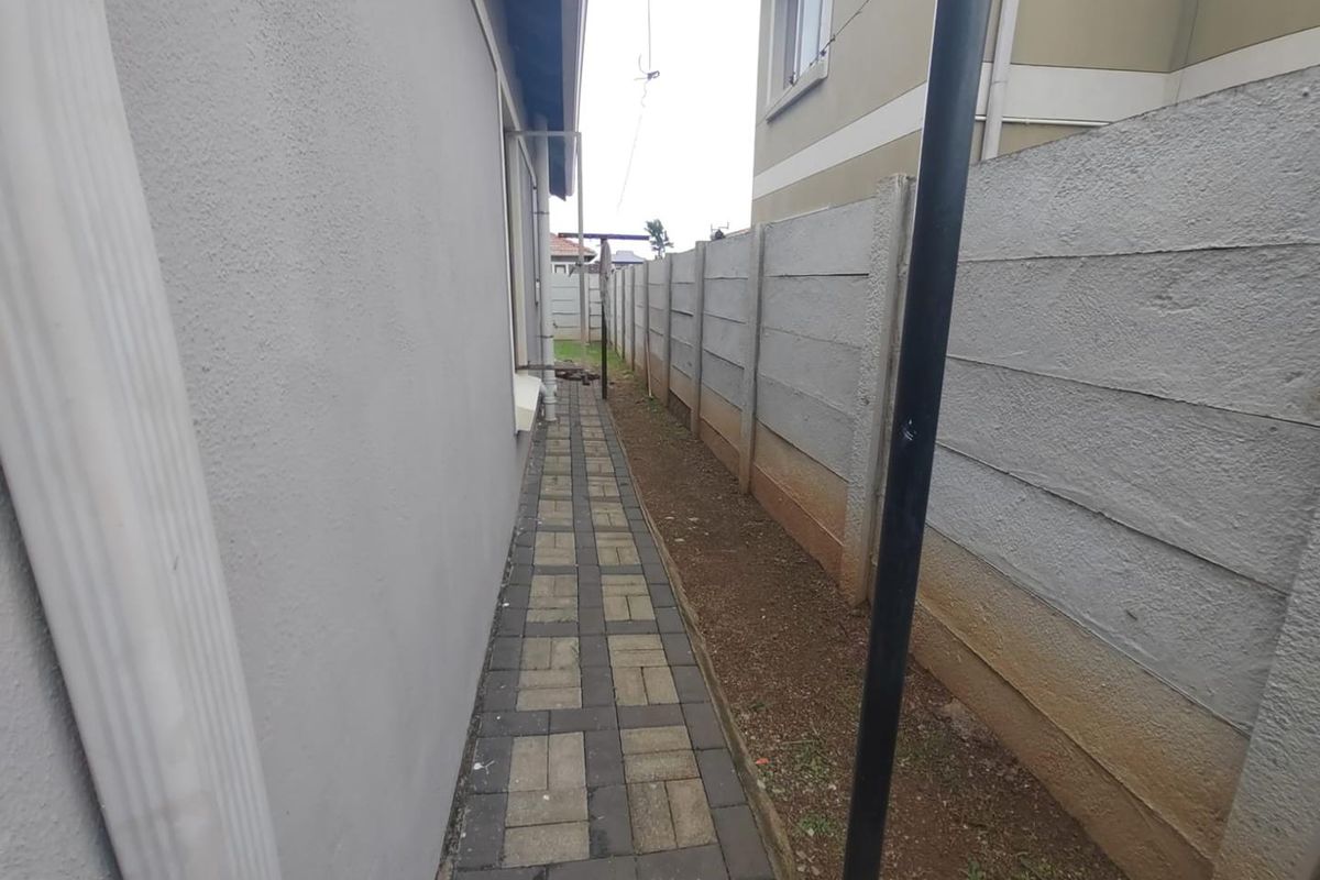 A narrow side passage featuring a paved walkway alongside a precast concrete boundary wall and exterior house wall.