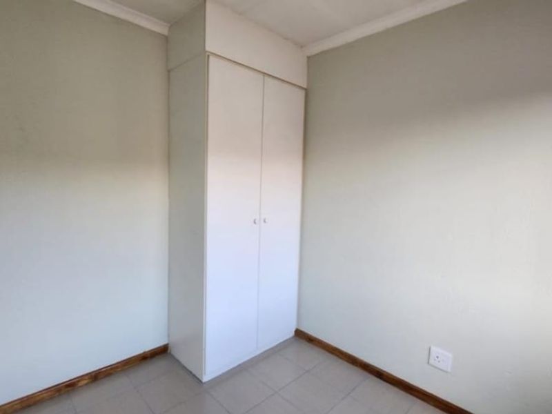 A clean, empty bedroom featuring neutral walls, tiled flooring, and a functional built-in cupboard for storage.