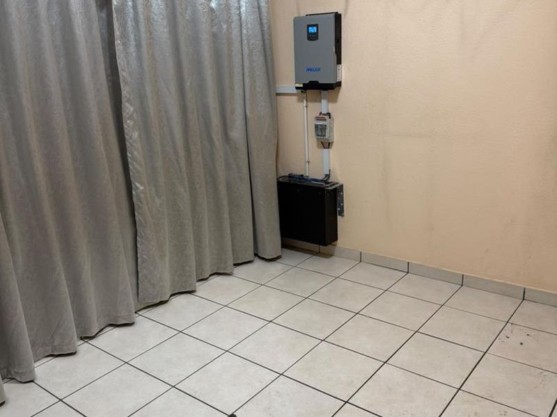 Utility space featuring tiled flooring and installed solar power infrastructure, including an inverter and battery unit.