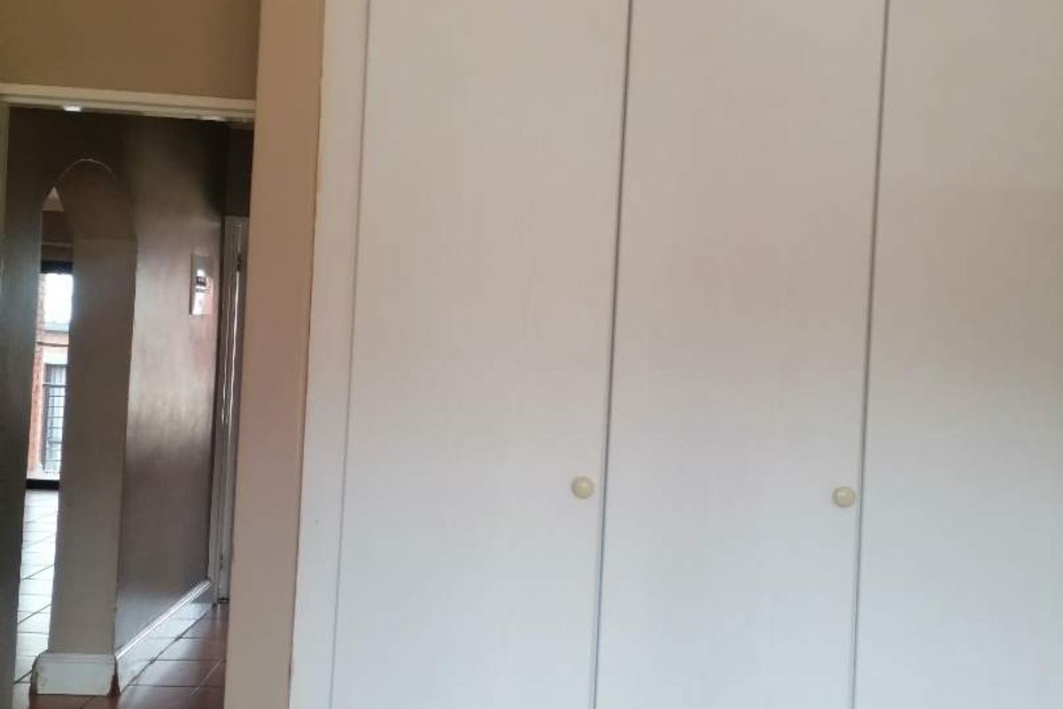 A bedroom interior featuring built-in wardrobes with white doors, coving, and carpet flooring, leading to a hallway with tiled floors.