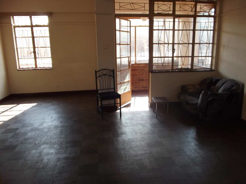 Spacious living area featuring original parquet flooring, large steel-framed windows, and direct access to an enclosed balcony area.