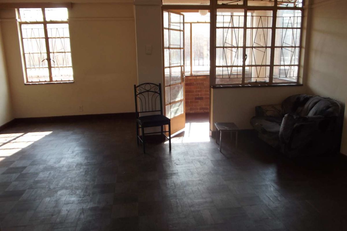 Spacious living area featuring original parquet flooring, large steel-framed windows, and direct access to an enclosed balcony area.