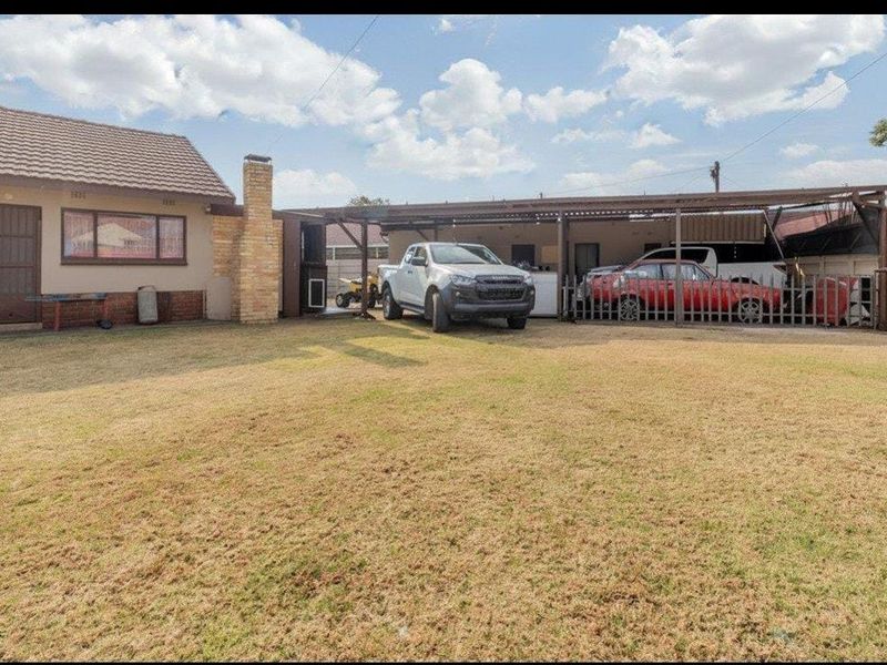 Spacious rear garden featuring a large lawn area, a brick chimney, and an extensive covered carport structure for vehicle storage.