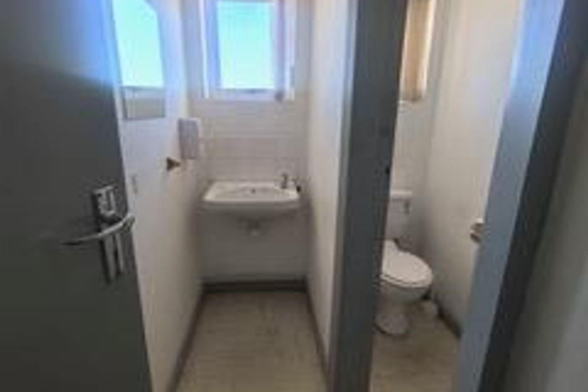 A functional bathroom featuring a wall-mounted basin and a separate toilet area with tiled flooring and natural light.