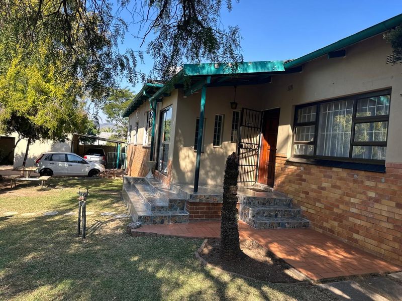 Front exterior view of a brick house featuring a covered tiled patio, security gate, and established garden area.