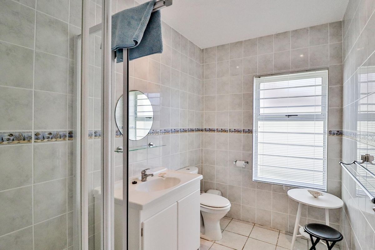 A functional bathroom featuring a glass-enclosed shower, vanity basin, and toilet, finished with neutral wall tiling and a window for natural light.