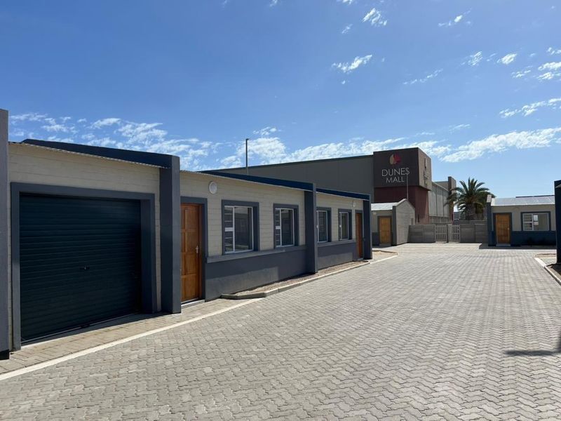 Exterior view of a townhouse complex featuring paved driveway access, roller garage doors, and modern timber entrance doors with aluminium window frames.
