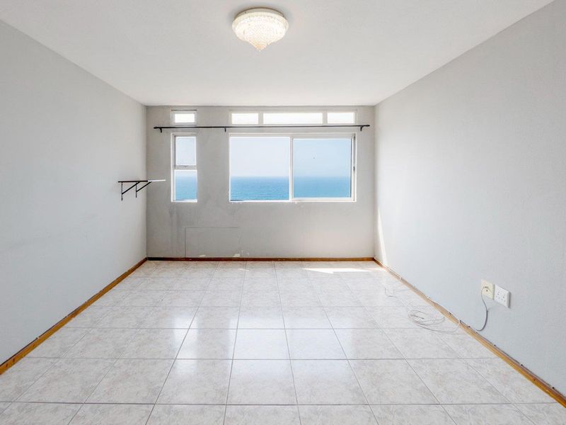 An empty bedroom featuring tiled flooring, a ceiling light fixture, and a window with a direct ocean view.