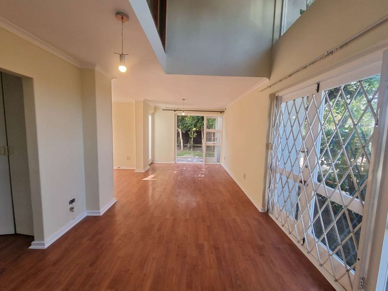 Spacious, empty living area featuring laminate flooring, neutral walls, and a sliding glass door with a security gate leading to the rear garden.