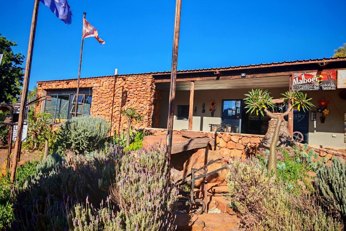 Front elevation of a rustic mixed-use building featuring natural stone cladding, a covered veranda, and corrugated metal roofing.