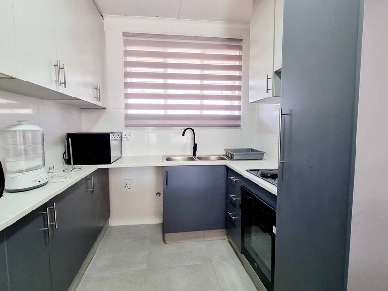 A compact kitchen featuring modern two-tone cabinetry, a double sink with a black mixer tap, built-in oven, and tiled flooring.