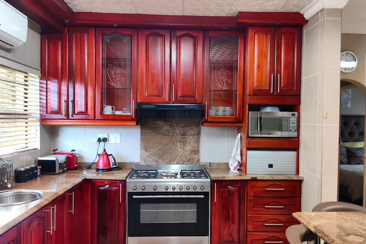 A functional kitchen featuring rich wood cabinetry, granite countertops, a built-in microwave, and a stainless steel gas stove with an extractor fan.