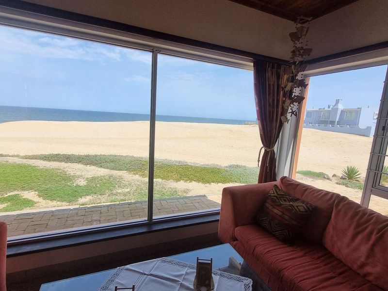 A bright living area featuring expansive floor-to-ceiling windows that offer panoramic views of the beach and ocean.