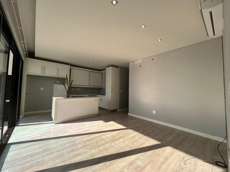Open-plan living area featuring laminate flooring, recessed lighting, a split-system air conditioner, and a modern kitchen with a central island.