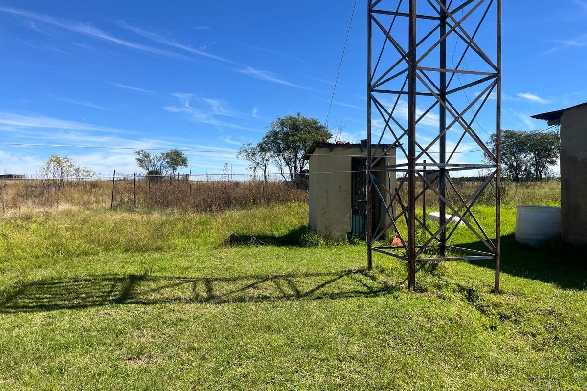 Exterior view of a farm property featuring a metal utility tower and a small outbuilding situated on open grassland.