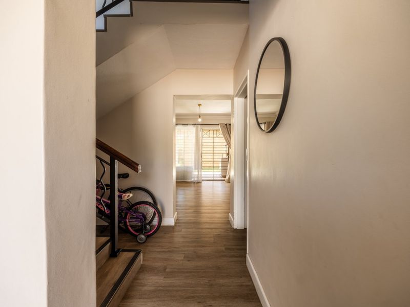 A bright hallway featuring laminate flooring and a staircase with a wooden handrail, leading through to an open living space.