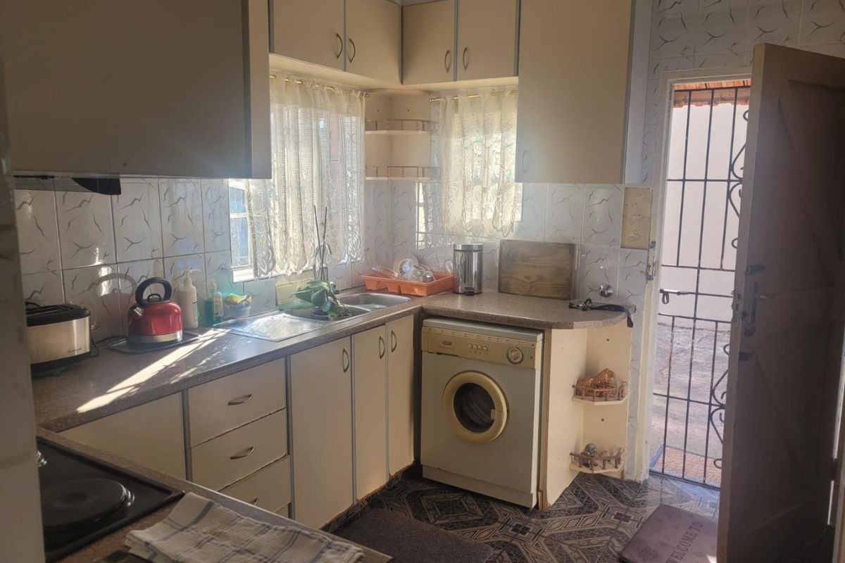A functional kitchen featuring laminate countertops, built-in cabinetry, and an integrated washing machine, with direct access to the exterior via a security gate.