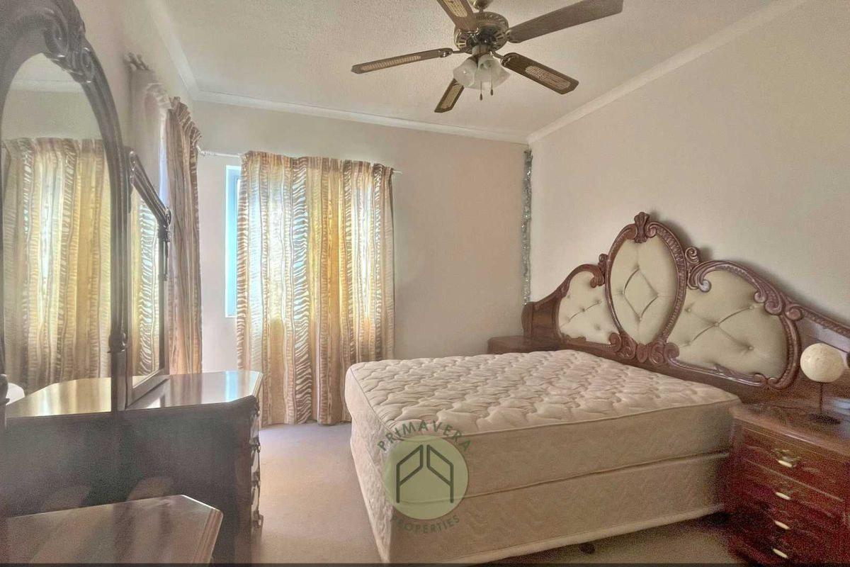 A spacious bedroom featuring neutral wall tones, carpeted flooring, and a ceiling fan, offering a comfortable and functional living space.