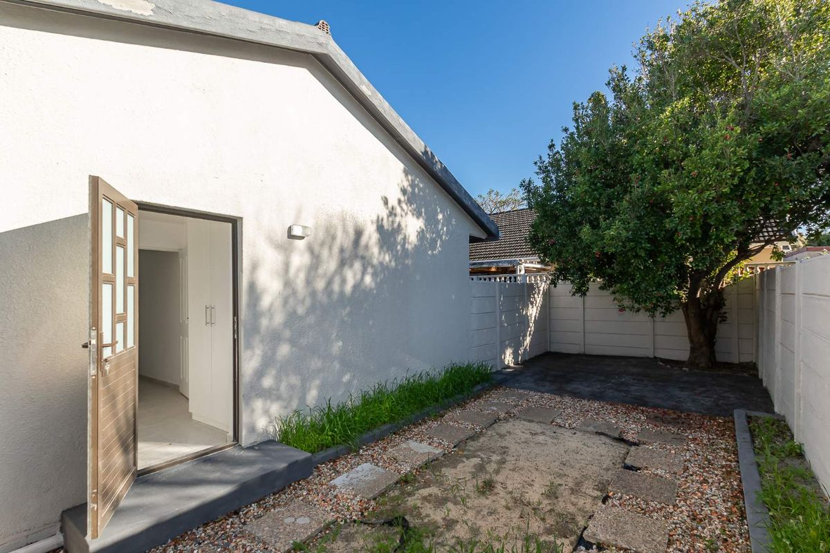A rear exterior view showing a paved garden area, precast boundary wall, and access to the interior through a hinged door.