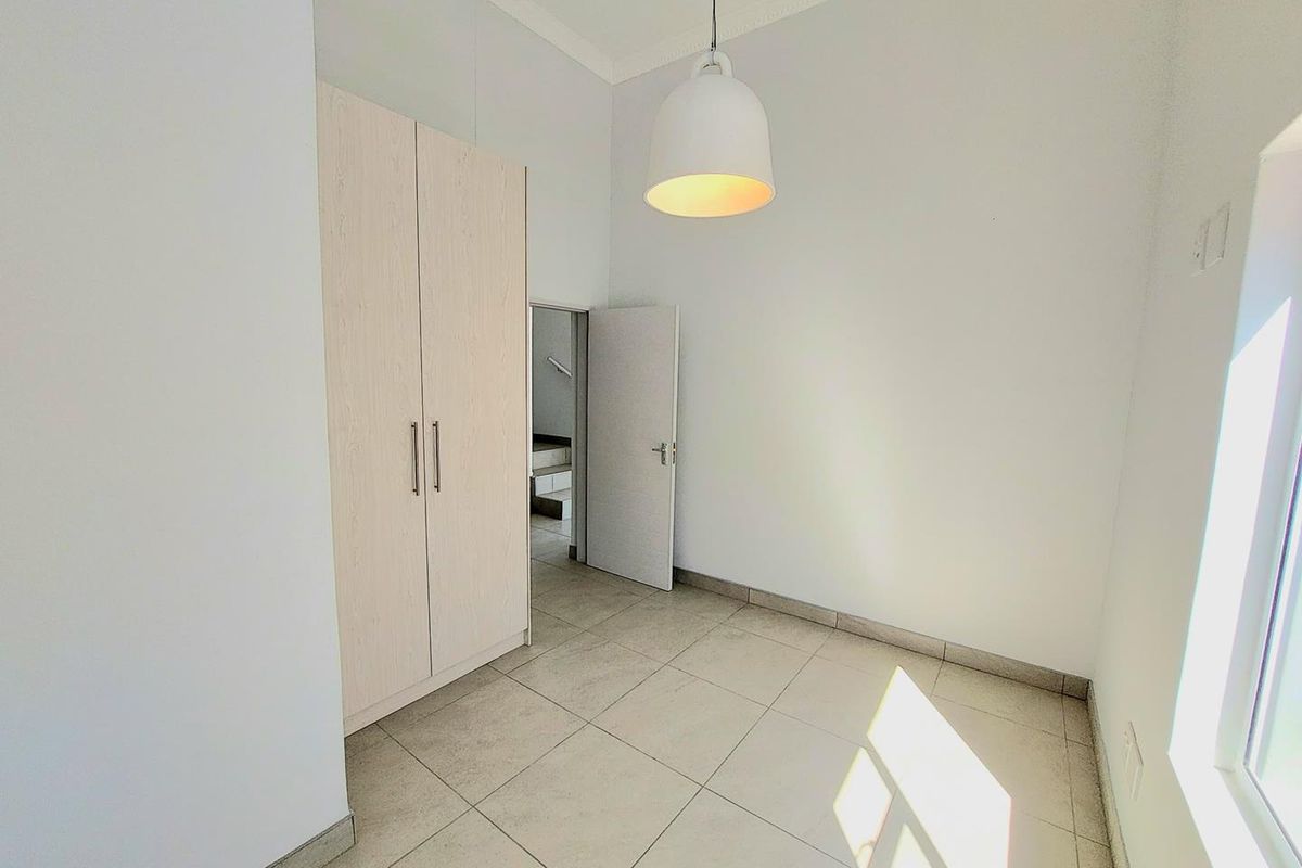 A bright, empty bedroom featuring neutral floor tiles, a built-in wardrobe, and a modern pendant light fixture.