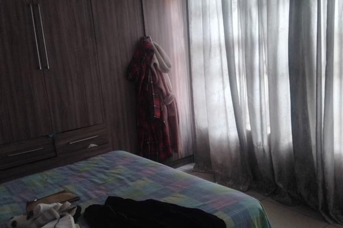 A bedroom featuring built-in wooden cupboards, tiled flooring, and large windows with curtains, providing a functional and well-structured living space.