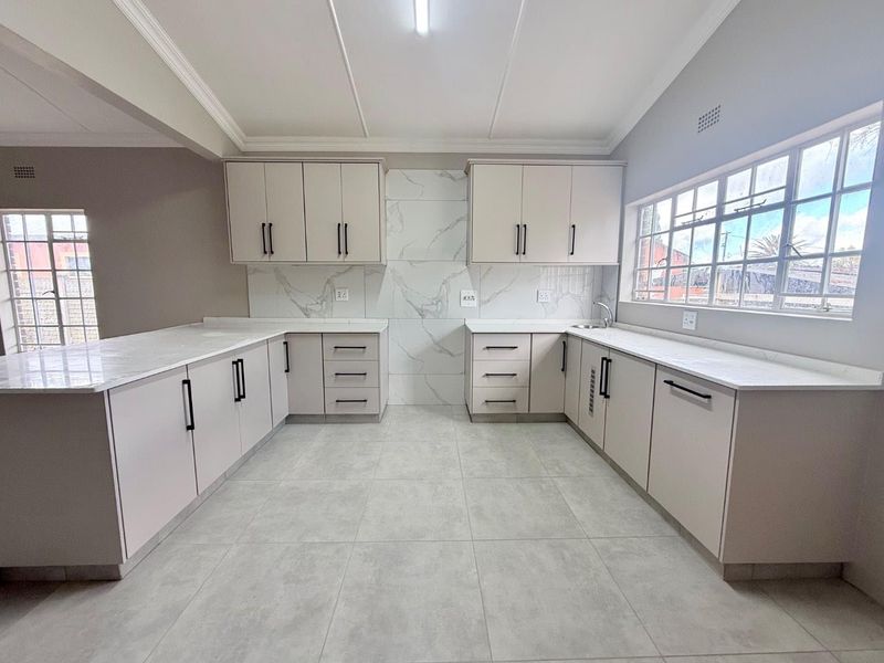 A modern, renovated kitchen featuring neutral cabinetry, stone countertops, marble-look splashback, and large format floor tiles in a bright, open-plan layout.