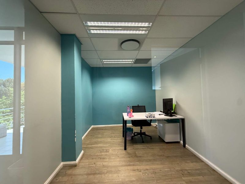 A professional office space featuring laminate flooring, a suspended ceiling with recessed lighting, and a modern glass partition wall.