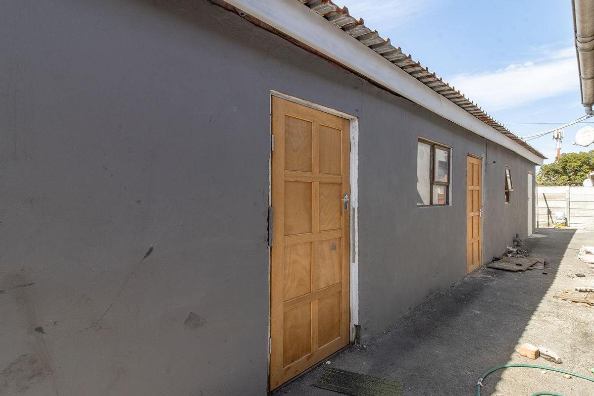 Rear exterior view of the property featuring a concrete pathway, timber doors, and corrugated metal roofing.