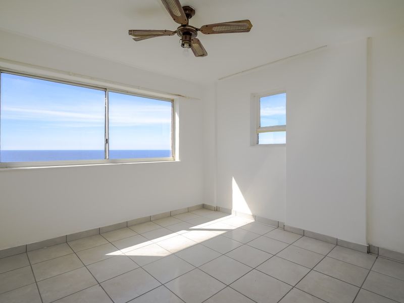 An empty bedroom featuring tiled flooring, a ceiling fan, and large windows offering expansive ocean views.