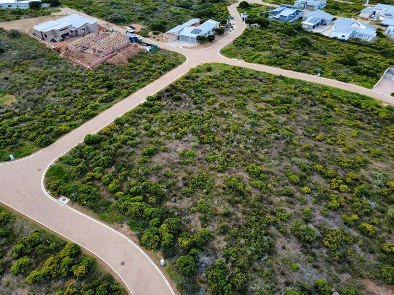 Aerial view of a vacant residential plot within a developed estate, featuring established paved road access and surrounding natural vegetation.