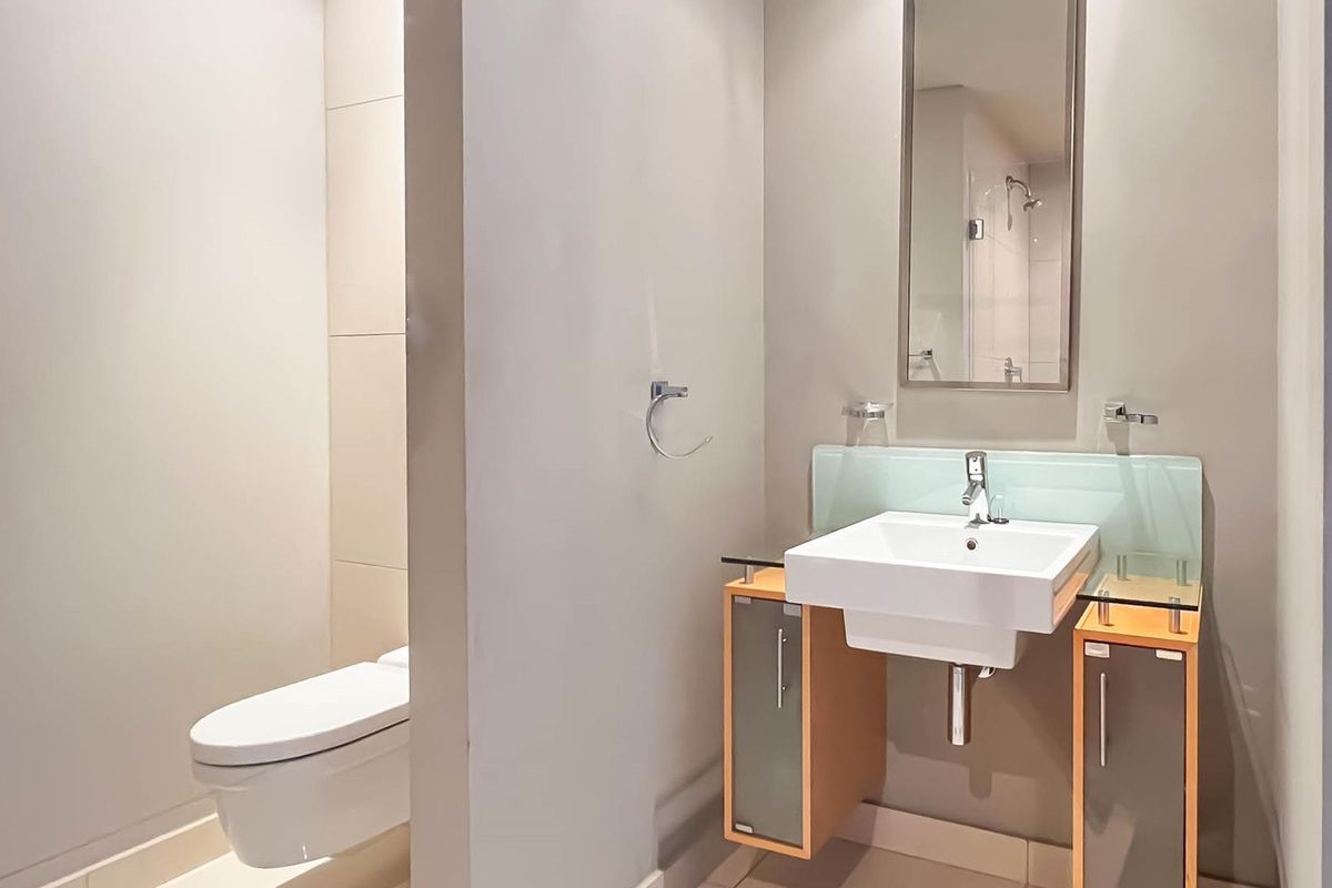 A modern bathroom featuring a wall-mounted vanity with a basin, a mirror, and a separate toilet area with tiled finishes.