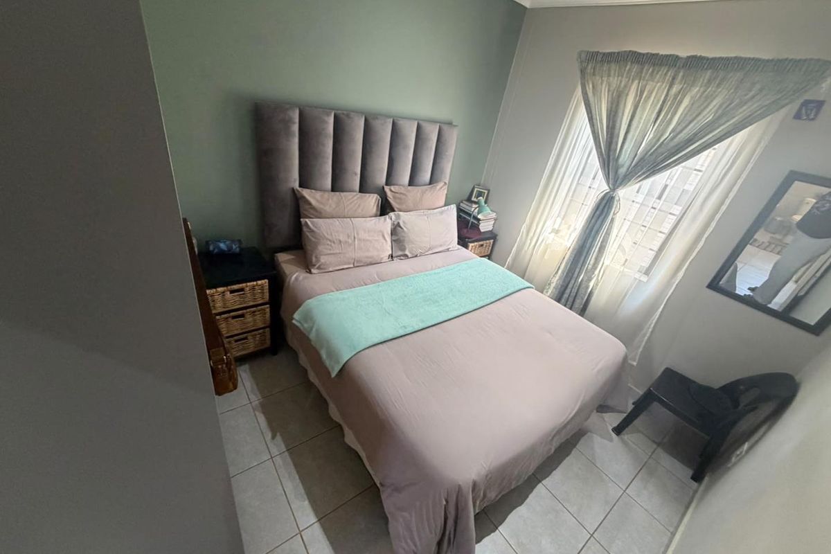 A well-maintained bedroom featuring tiled flooring, crown molding, and a neutral color palette with an accent wall.