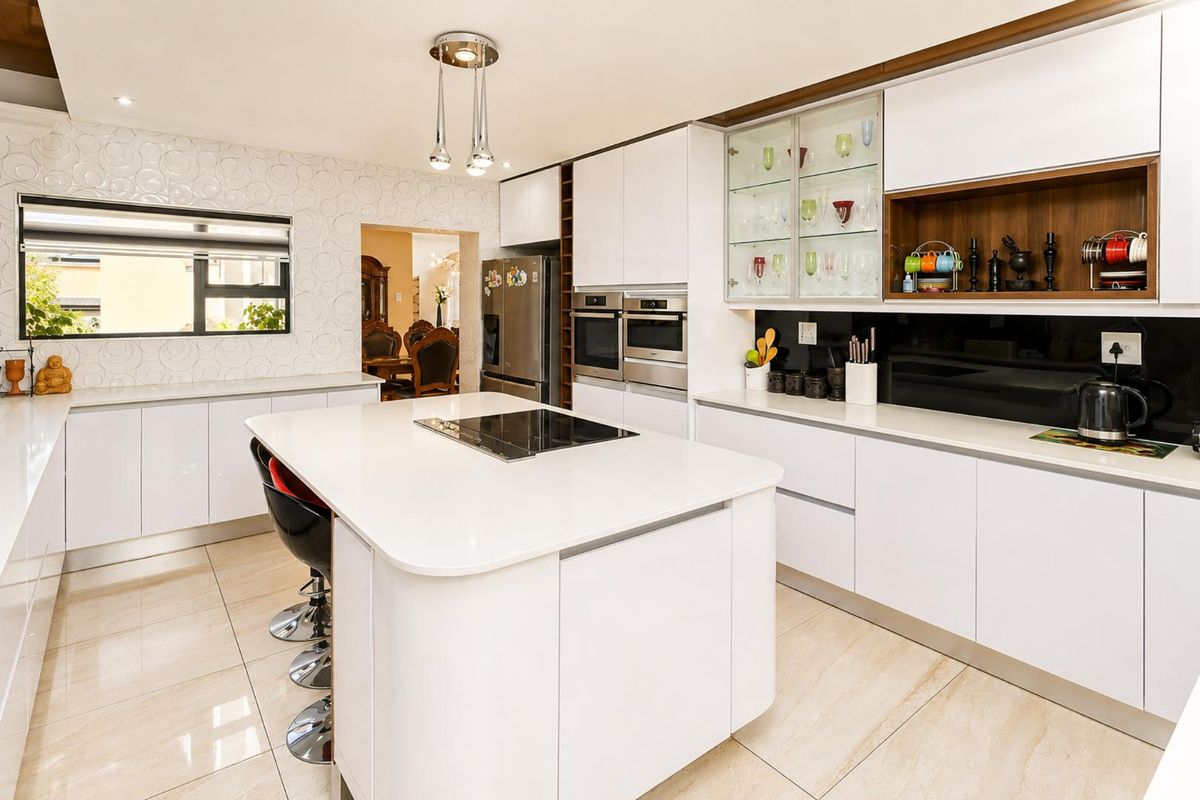 Modern kitchen featuring a central island with induction hob, sleek white cabinetry, built-in double ovens, and high-quality tiled flooring.