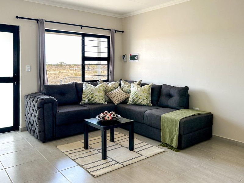 A bright and modern living room featuring neutral tiled flooring, large windows with security bars, and direct access to the exterior via a glass door.