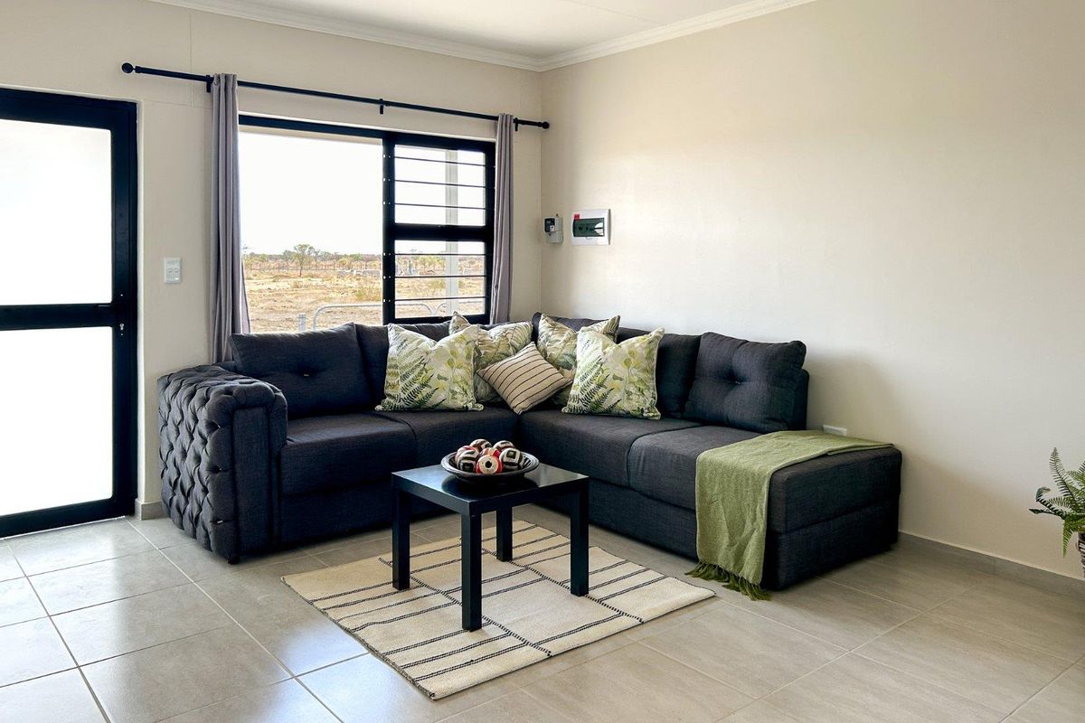 A bright and modern living room featuring neutral tiled flooring, large windows with security bars, and direct access to the exterior via a glass door.