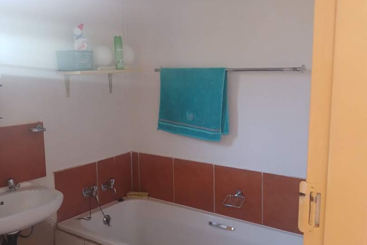 A functional bathroom featuring a built-in bathtub with tiled surround, a wall-mounted basin, and chrome towel rail.