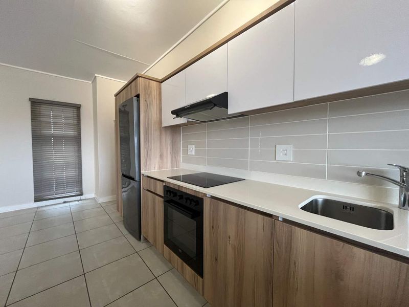Modern kitchen featuring wood-grain and white cabinetry, stone countertops, integrated electric hob, oven, extractor fan, and a stainless steel sink.