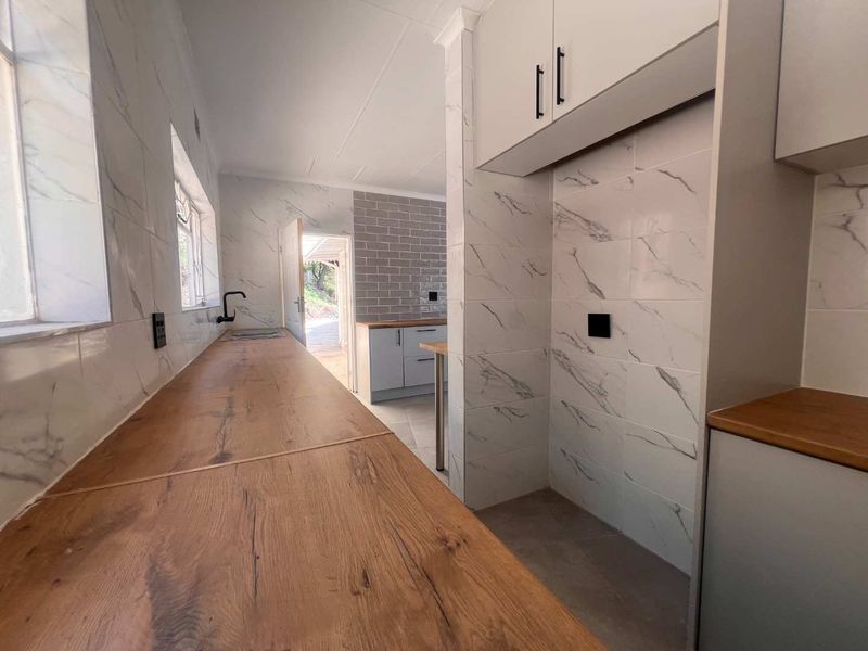 A modern, empty kitchen featuring marble-look wall tiles, wooden countertops, and grey subway tile accents, offering a clean and contemporary aesthetic.