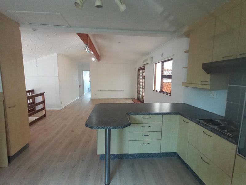 Spacious open-plan living area featuring a functional kitchen with built-in cabinetry, electric hob, and oven, flowing into a bright, neutral living space.