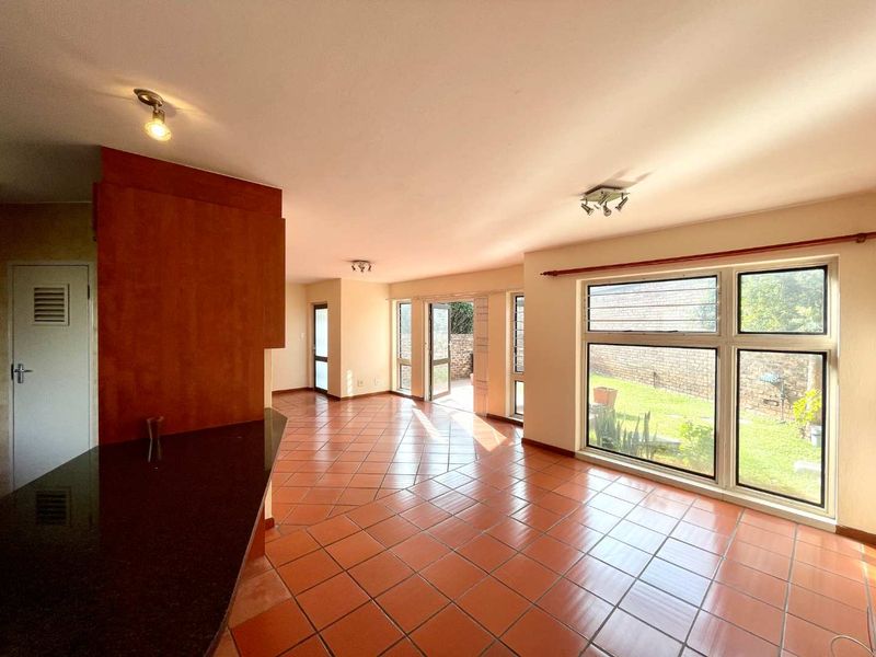 Spacious open-plan living area featuring terracotta floor tiles, granite kitchen counter, and large windows providing natural light and access to the rear garden.