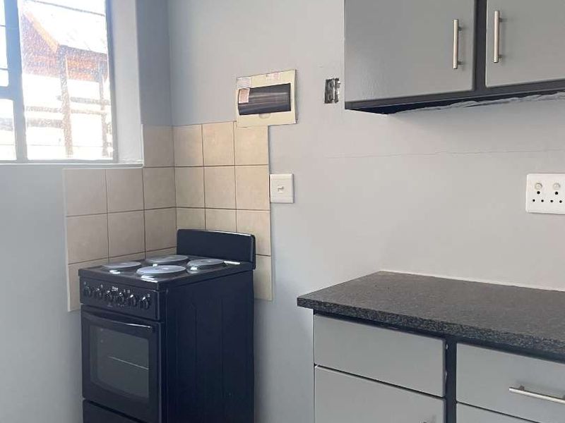 A functional kitchen featuring grey built-in cabinetry, a dark laminate countertop, tiled splashback, and a freestanding stove.