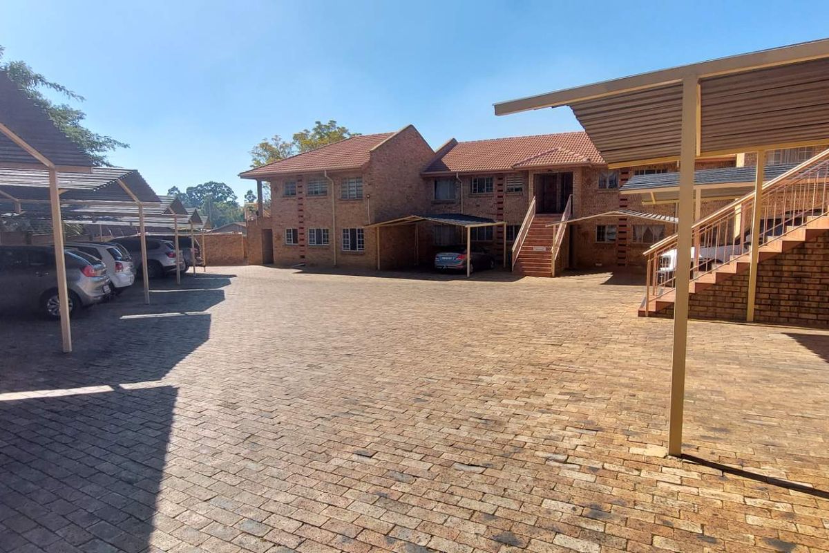 Exterior view of the apartment complex courtyard featuring paved parking areas, covered carports, and brick building facades with external staircases.