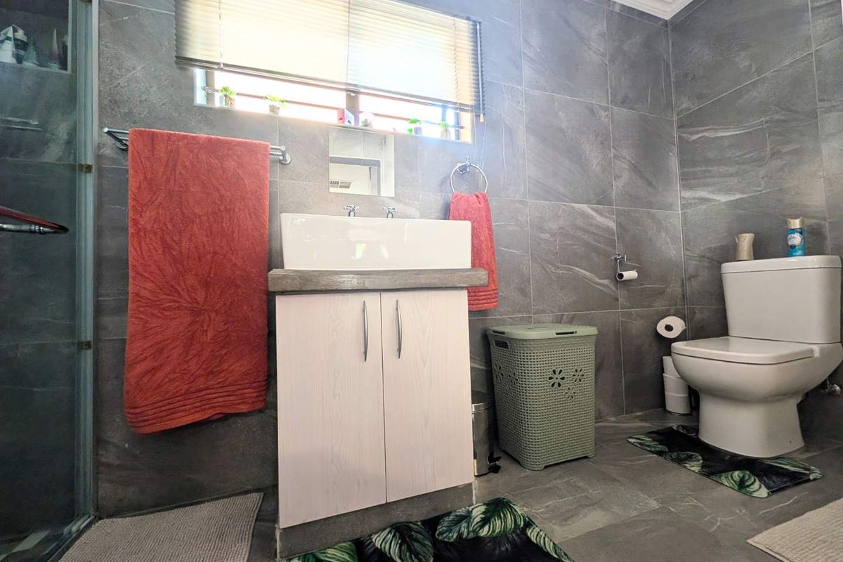 A modern bathroom featuring grey wall and floor tiles, a vessel sink with a vanity cabinet, a toilet, and a glass-enclosed shower.