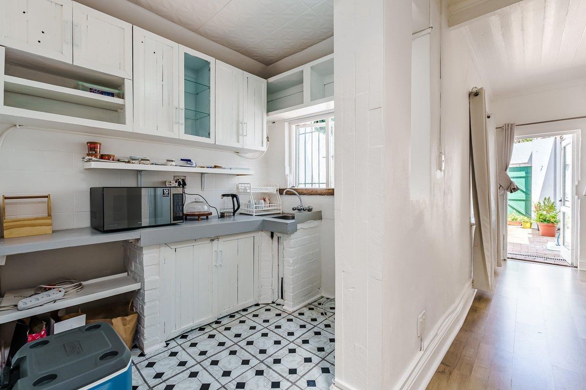 A compact kitchen area featuring white cabinetry, a stainless steel sink, and patterned tile flooring, leading through to an outdoor patio space.