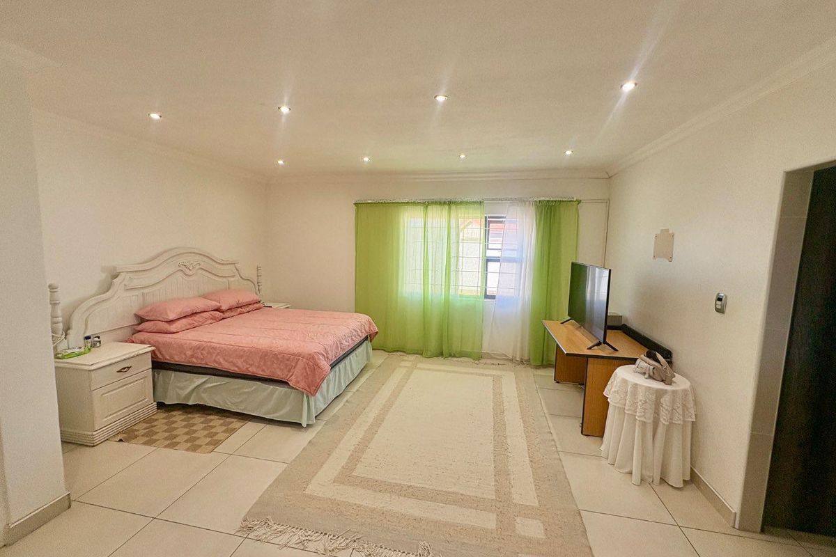 Spacious bedroom featuring neutral floor tiles, recessed ceiling downlights, and a large window with natural light.