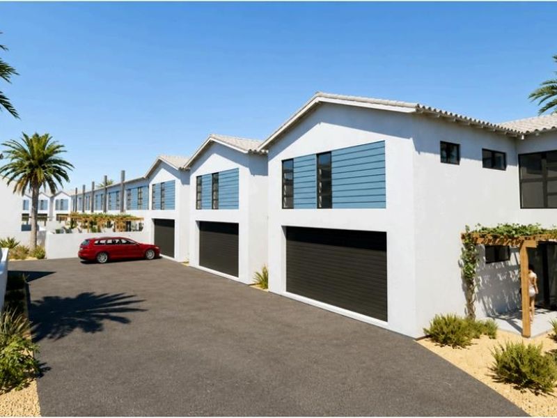 A modern townhouse complex featuring white facades, dark garage doors, tiled roofs, and timber pergolas, set along a paved driveway.