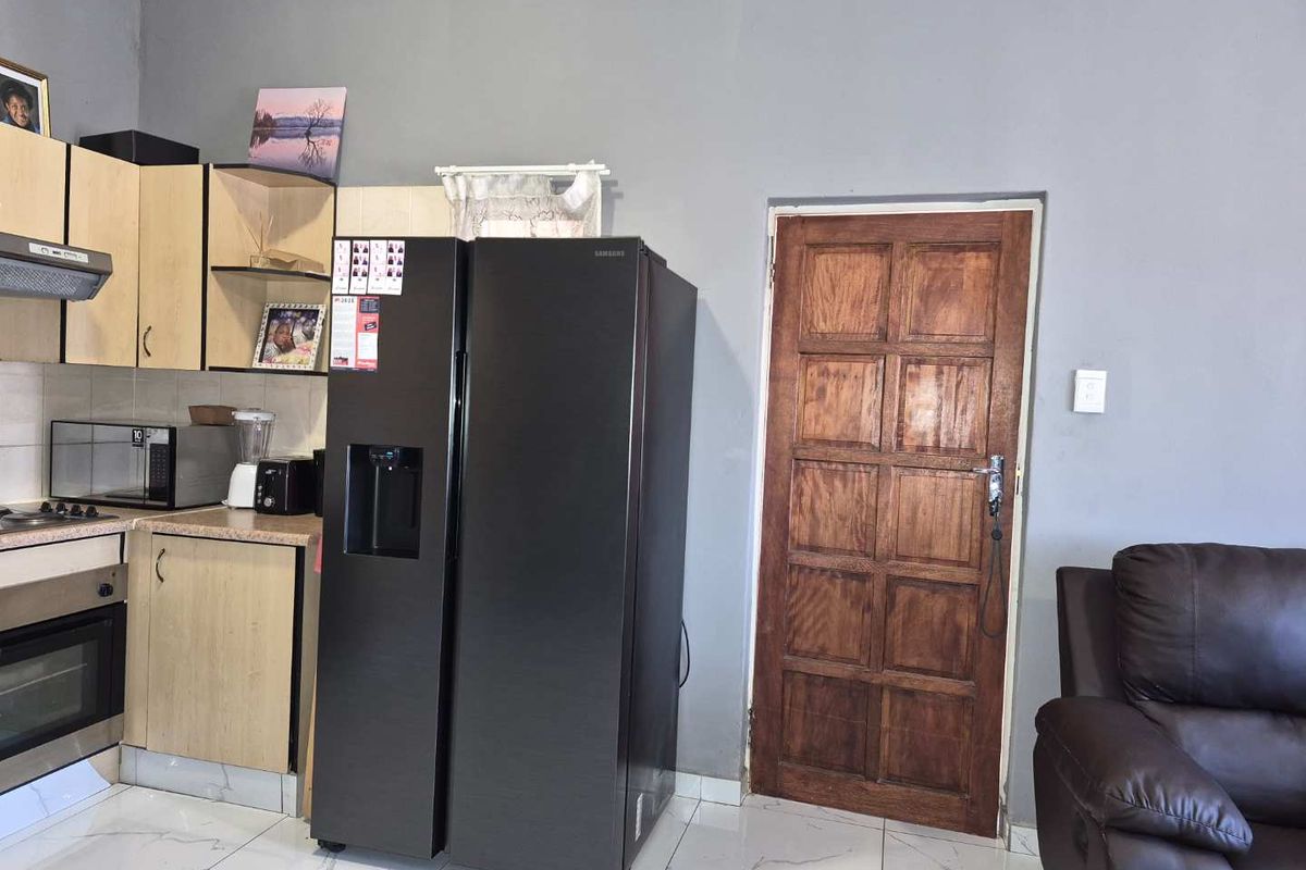 A functional kitchen area featuring light-toned cabinetry, built-in oven and hob, extractor fan, and modern tiled flooring, adjacent to a wooden door.