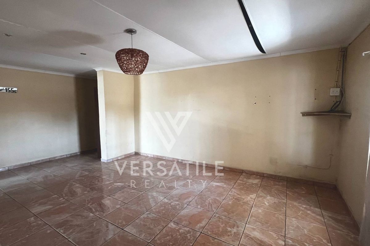 An empty living area featuring tiled flooring, neutral walls, and a central pendant light fixture, offering a blank canvas for personalization.