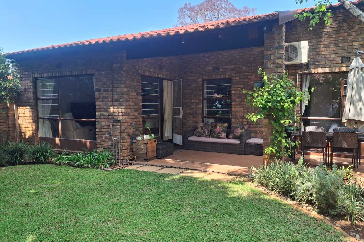 Rear view of the townhouse featuring a covered patio area, exposed brick exterior, and a well-maintained garden space.